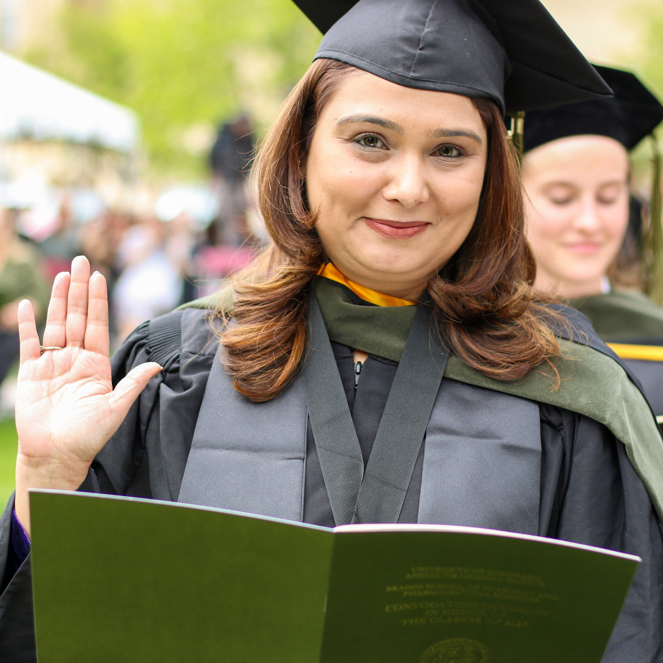 Woman wearing cap and gown with hand up