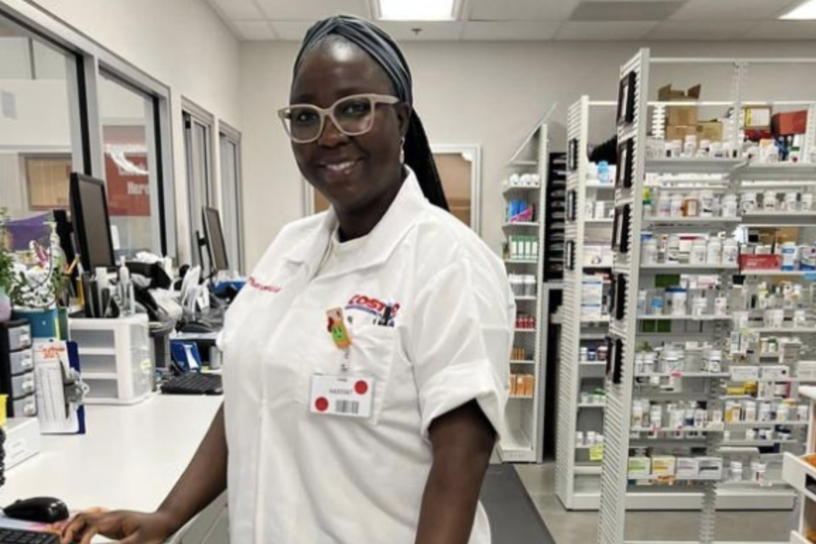Woman at costco pharmacy with shelves of medication in the back