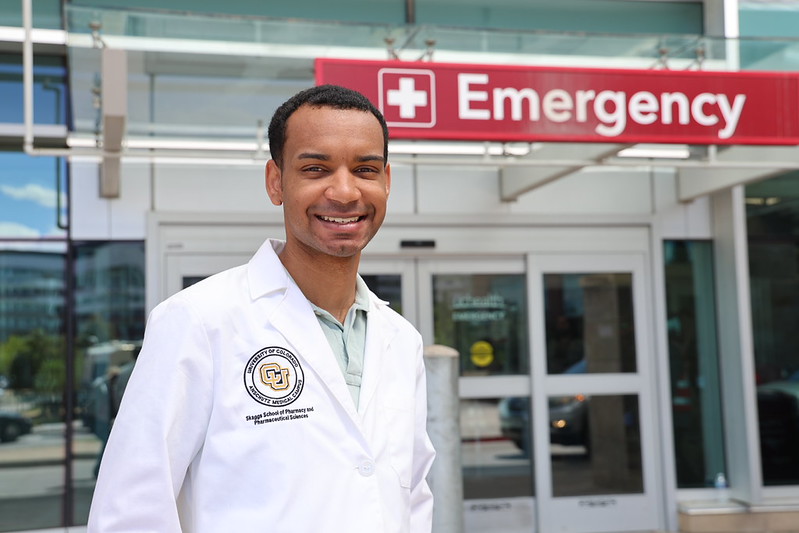 Student wearing white coat in front of UCHealth emergency sign