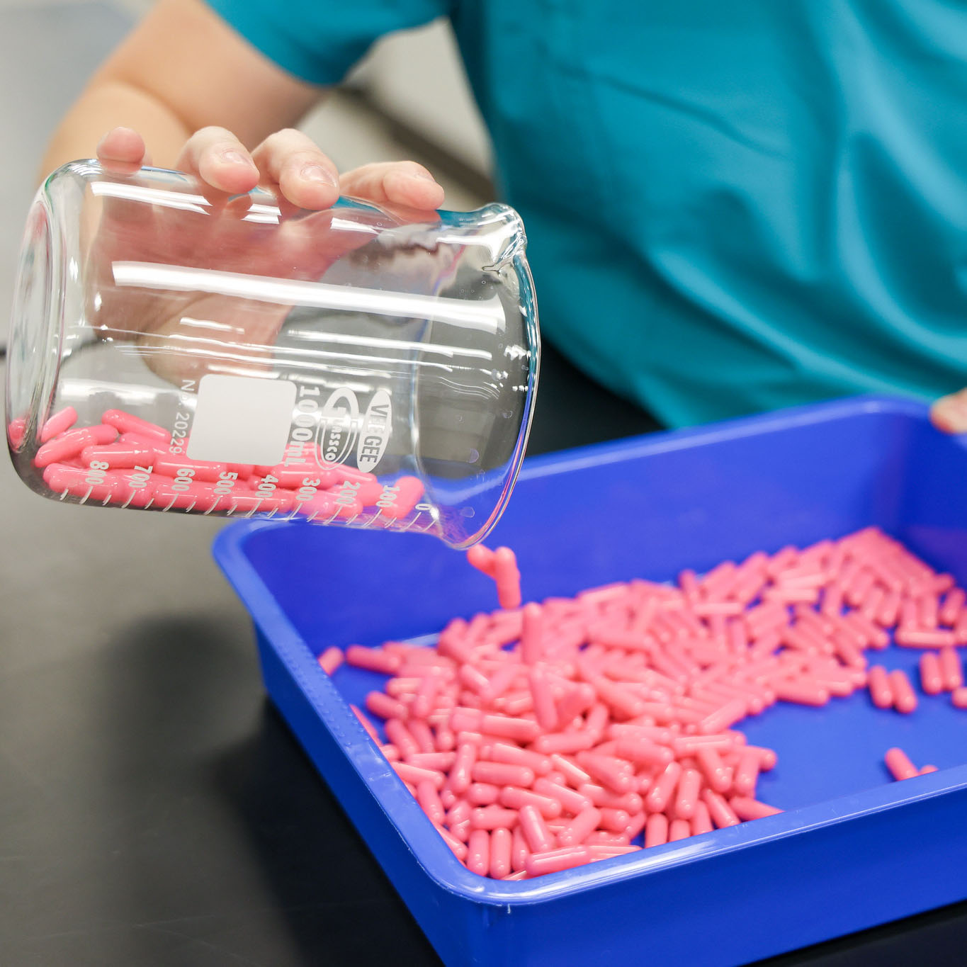 Person counting pink pills in a blue container 