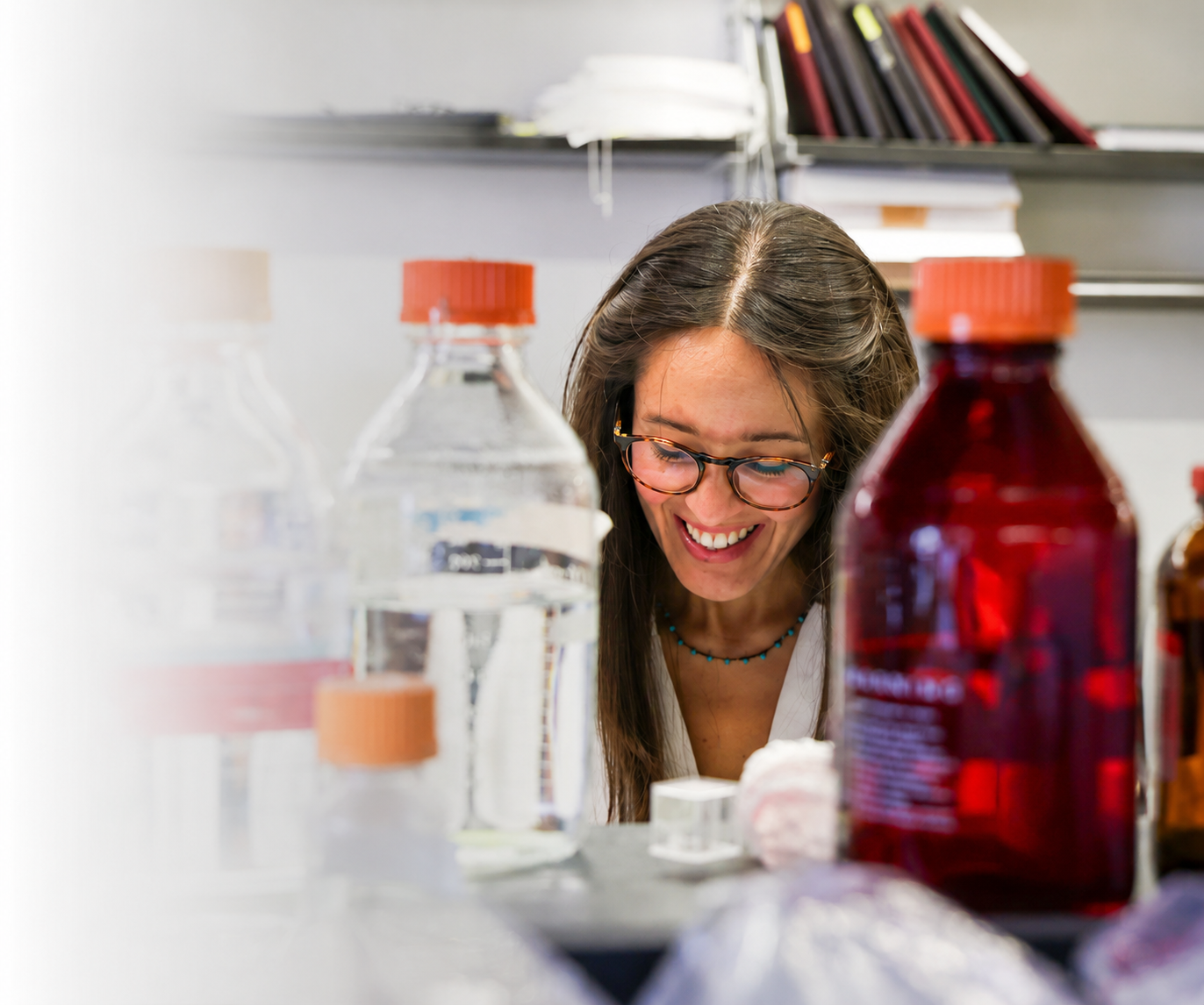 Smiling scientist wearing glasses works among laboratory bottles and equipment.