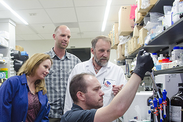 Group of students and faculty looking at beaker.